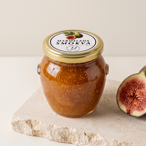 Staklenka marmelade od smokve MAGICA, s etiketom na zlatnom poklopcu, uz prepolovljenu smokvu.